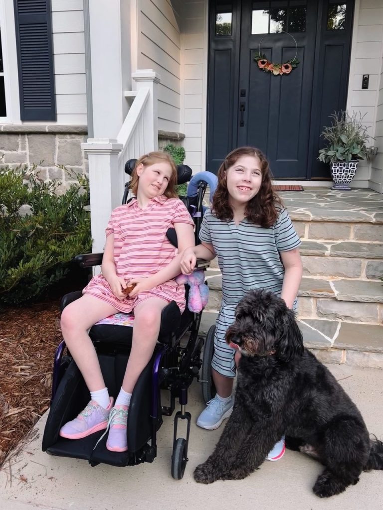 Amelia and Makenzie Kahn outside the front entrance of a home with their dog Pongo